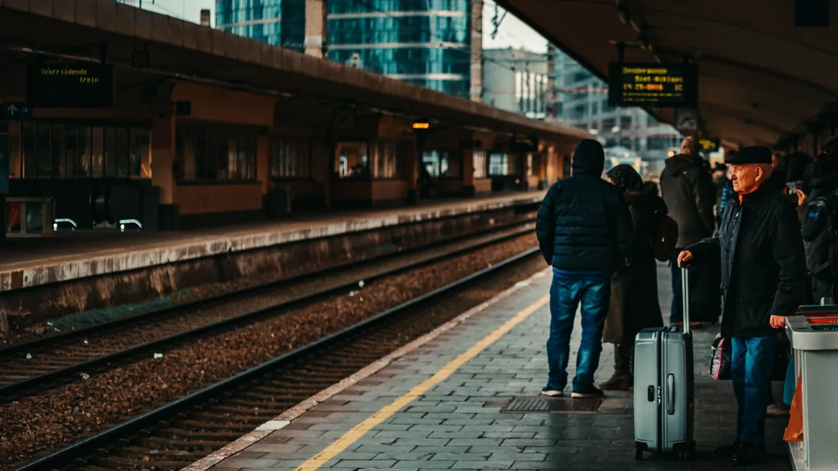 Viaggiatori con bagagli sui binari di una grande stazione ferroviaria italiana